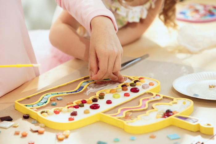 Μικρό κορίτσι με τη βοήθεια ενήλικα, κάνουν κολάζ με αντικείμενα. Φαίνονται μόνο χέρια όχι πρόσωπα.